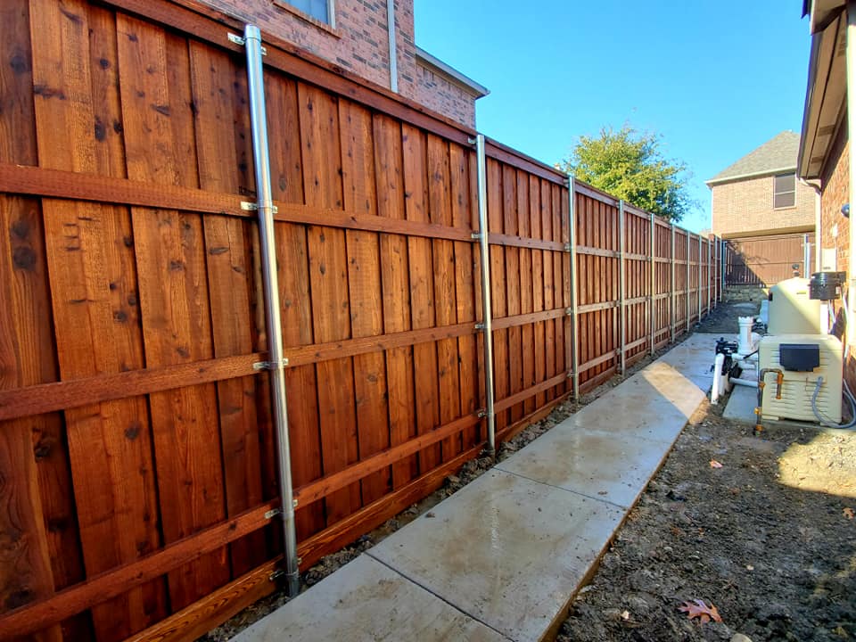 "A stunning cedar fence featuring a vertical design, standing tall at 8ft, surrounded by greenery, adding charm and privacy to the backyard space."
